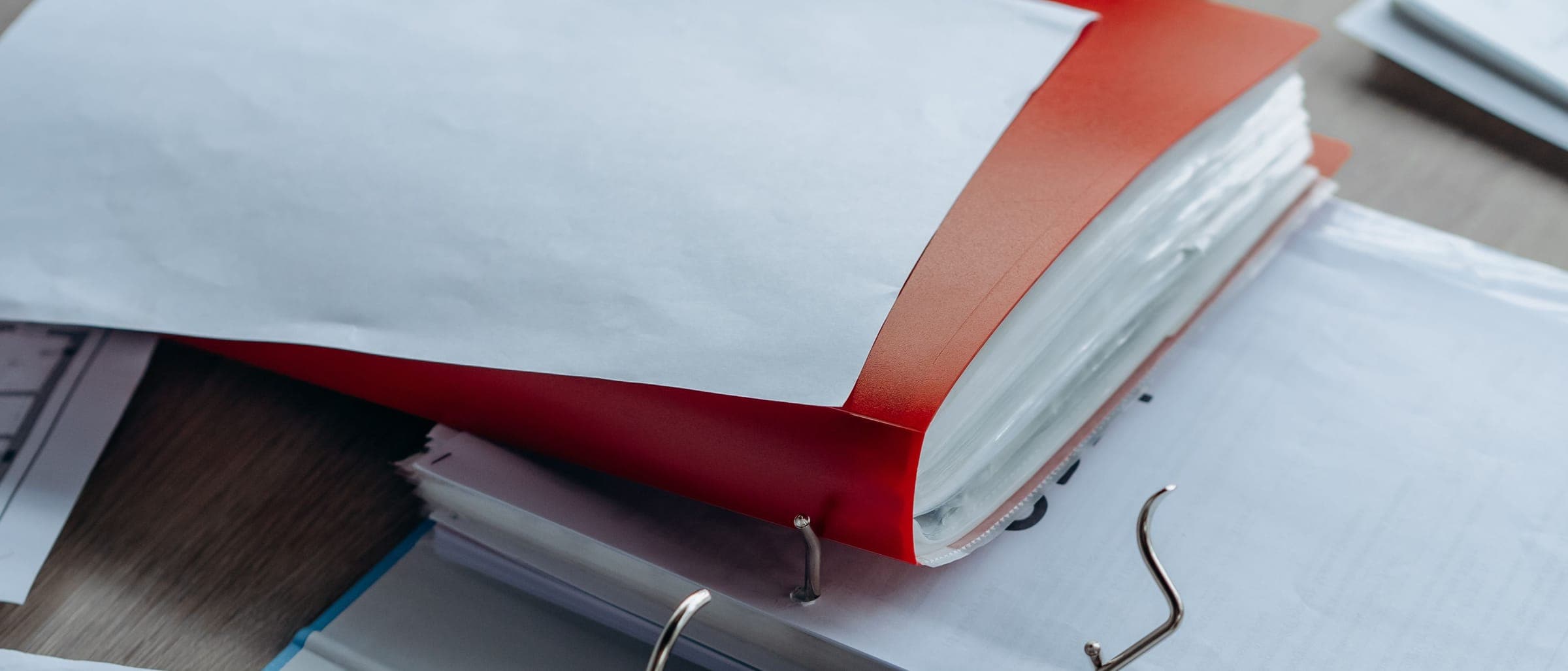 A red folder and stacks of paper lying on an open ring binder on a desk